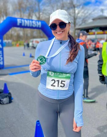 Person in athletic wear and cap holding medal, standing by finish line at an outdoor race event