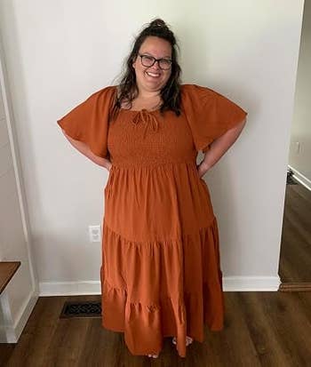 Person smiling in a flowing, tiered dress with puff sleeves, standing in a room with hands on hips
