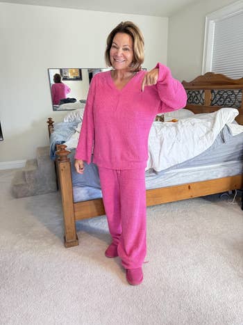 Person in cozy, textured loungewear set standing in a bedroom, smiling and gesturing towards outfit