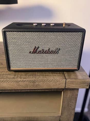 Marshall Bluetooth speaker on a wooden surface, showcasing a vintage design with a metal grille and control knobs on top