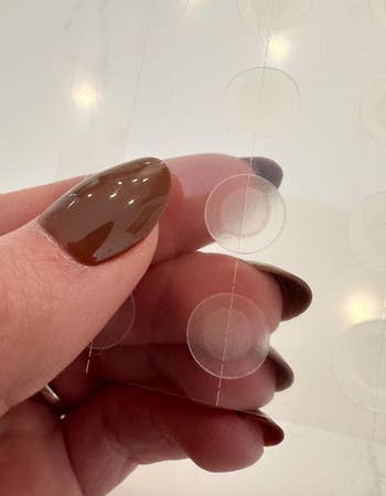 Hand holding transparent adhesive circles, possibly acne patches