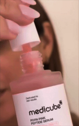 A person applies serum from a medicube bottle with a dropper. The focus is on the product bottle and application