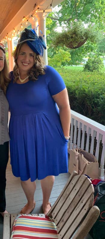 Two people smiling on a porch. One wears a ruffled top and pants; the other a blue dress with a matching fascinator, suitable for a social gathering