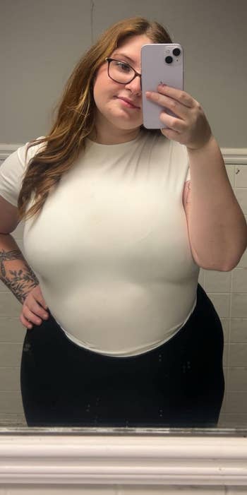Person taking a mirror selfie in casual white top and black pants
