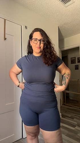 Person in casual, form-fitting activewear with short sleeves and shorts, standing in a home setting
