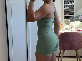 Person in form-fitting athletic wear poses in a room with a vanity and mirror