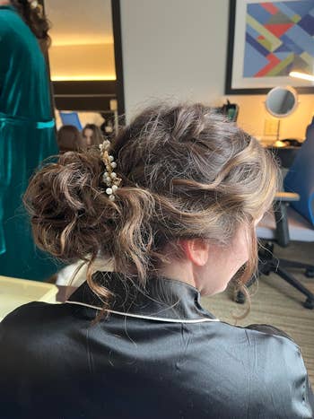 A reviewer with an intricate updo hairstyle adorned with pearls, wearing a satin robe, seated in a room with a mirror and abstract art on the wall