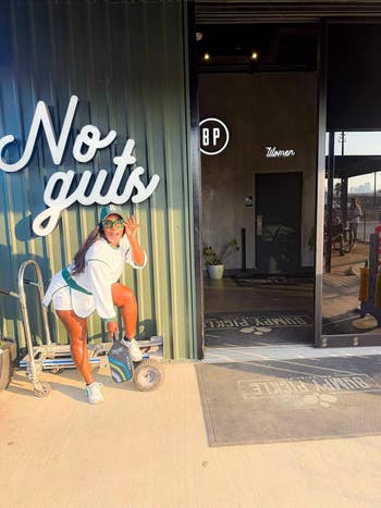 Person in casual shorts and a cap poses playfully