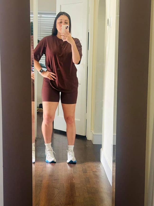 Person taking a mirror selfie in a matching t-shirt and shorts outfit with sneakers in a home setting