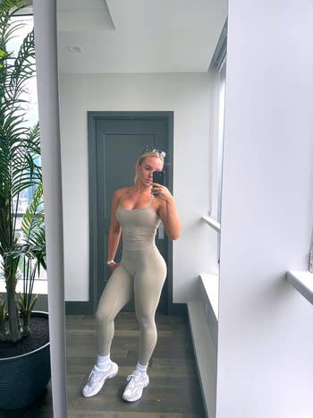 Person in form-fitting activewear takes a mirror selfie in a modern room with large plant and windows