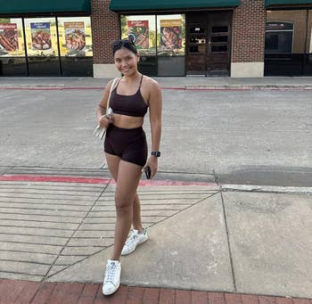 Person in athletic wear stands outside, holding a purse and wearing sneakers