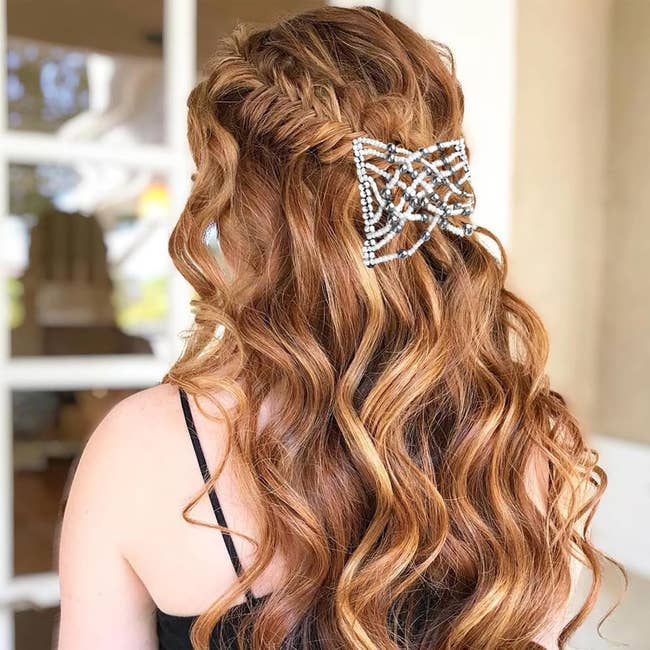 model with long wavy hair adorned with a decorative rhinestone hair clip shaped like a bow, wearing a black strap dress