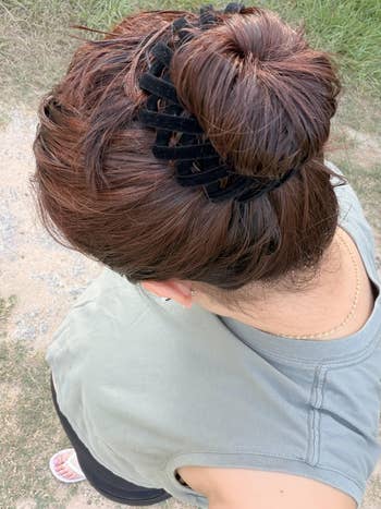Top view of a reviewer with brown hair styled in a bun secured with a large black hair clip, wearing a sleeveless top and a thin necklace