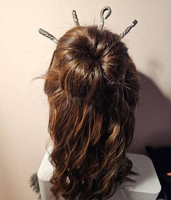 Back view of a reviewers styled hair mannequin with wavy hair adorned with decorative hair sticks